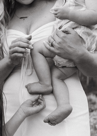 Mom holds her baby while her other child tickles the little baby's feet.