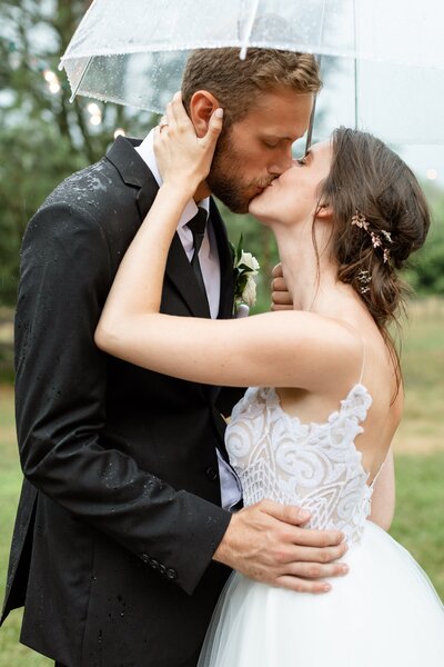 Carly  Caleb Arrowwood Farms Wedding Kissing under umbrella