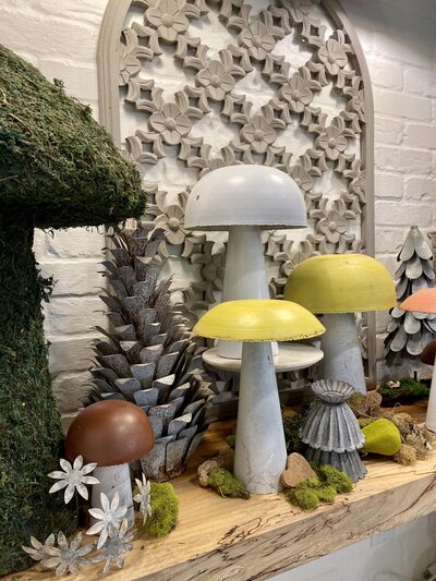Decorations on a shelf of metal mushrooms, moss pieces and a floral inspired carved wood panel in the background.
