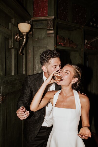 a groom kissing his bride during cake cutting .the bride is eating cake. direct flash shot