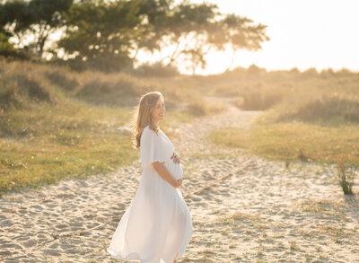 Expecting mother in flowing dress during golden hour beach maternity session in Sandbanks, Dorset