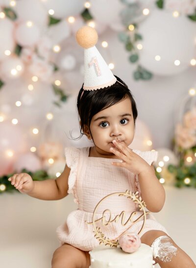 Baby girl eating cake in front of peach balloon garland. Cake smash photo taken by Jenni Nikki Photography in Atlanta, GA.