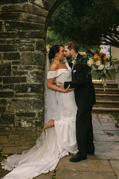 bride and groom kiss against brick wall