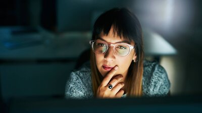 Focused woman in glasses analyzing content on screen during late work session.