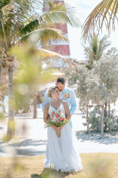 Newly weds at hteir wedding in the Bahamas by a lighthouse and plam trees by a destination wedding photographer