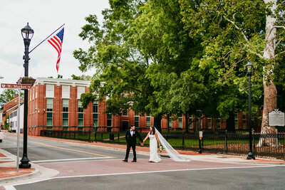 Eloping couple walking across crosswalk near historic red-brick Virginia courthouse with
flowing veil