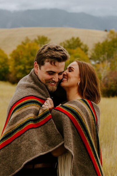 Couple smiles while wrapped  in a blanket for their Bozeman engagement session.