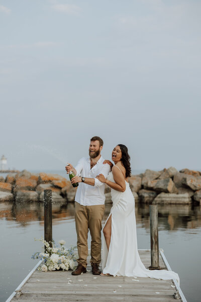 bride and groom spraying champagne on a dock over the water. captured by a Minnesota Elopement Photographer