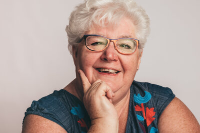 Headshot of a white haired woman with glasses. Very open and friendly., looks like she is listening . Headshots.  Branding photo.