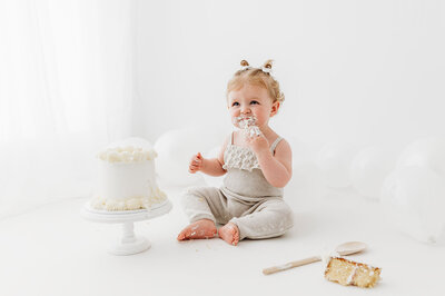 Cake smash, baby girl eating cake wearing beige romper on white background