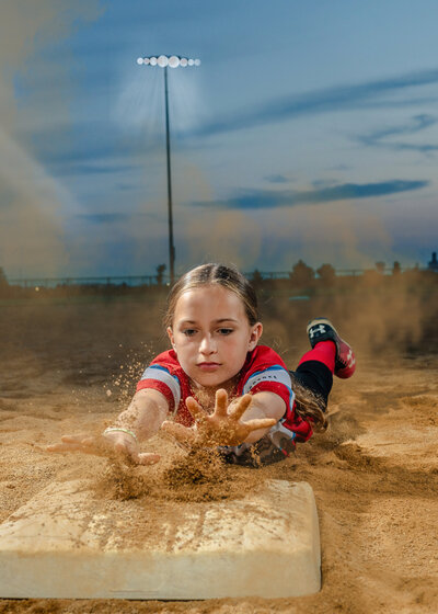 A young girl slides into a base as dirt flies around her. 