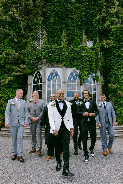 Photo of a groom and his groomsmen walking together towards the camera with Luttrellstown Castle in the background