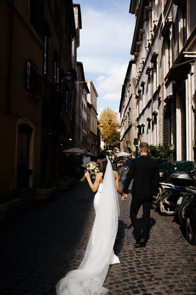 A bride and groom holding hands and walking down a cobblestone street.