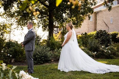 Photo by Chattanooga Wedding Photographer of a couple just before their first look, shot through some leaves. The bride is standing behind the groom both looking forward in anticipation