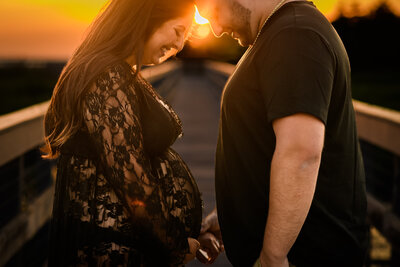 Expectant couple touching foreheads and holding hands, silhouetted by sunset during a maternity shoot