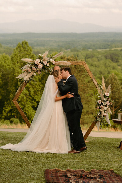 A couple kisses in front of the mountain backdrop at their ceremony.