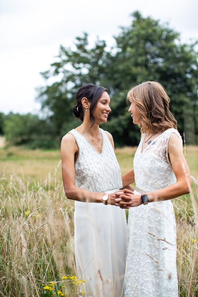 two brides smiling holding hands in long grass