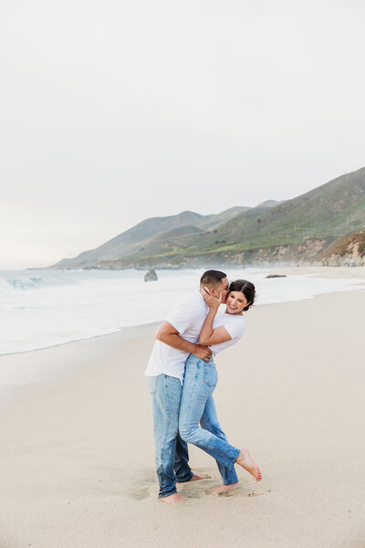 guy kisses fiance on the cheek on the beach