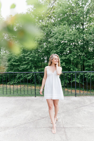 blonde girl wearing purple and blue dress posing under a tree