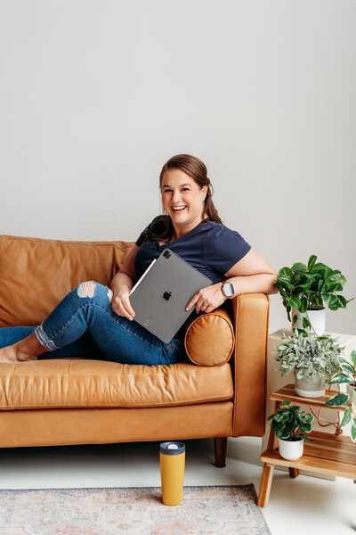 Woman sitting on a leather couch holding a laptop.