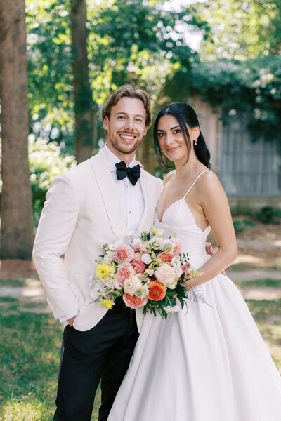 A bride and groom posing for photos on their wedding day at Wheatfield Estate with a colourful flower bouquet.