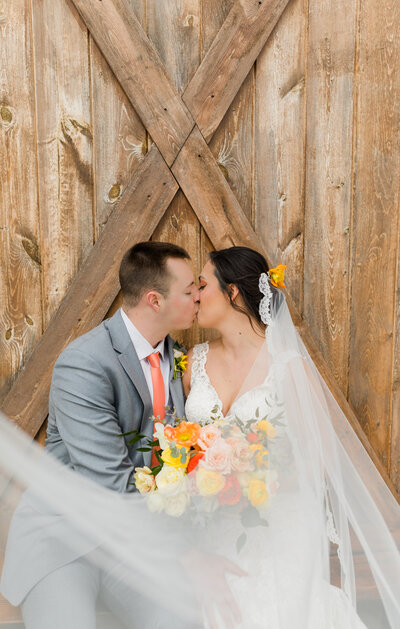 bride and groom kissing around veil