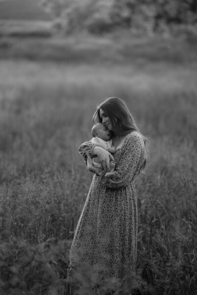 mother holding her newborn baby while standing in a field