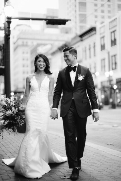 Black and white photo of bride and groom holding hands walking down the street