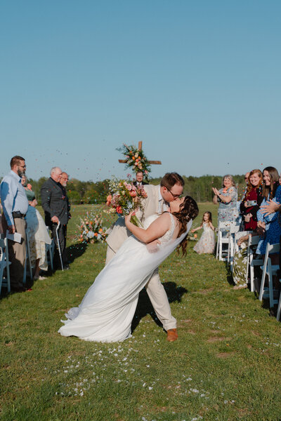 Colorful photo of groom dipping his bride while walking up the aisle and confetti is flying in the back