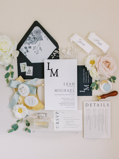 Flatlay of wedding details including invitation suite,  florals, perfume, name cards