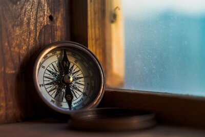 Brass compass resting on a sunlit wooden windowsill, symbolizing choosing your own path.