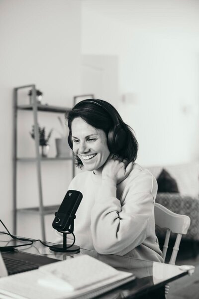 Black-and-white photo of Kaya smiling during a podcast recording, wearing headphones.