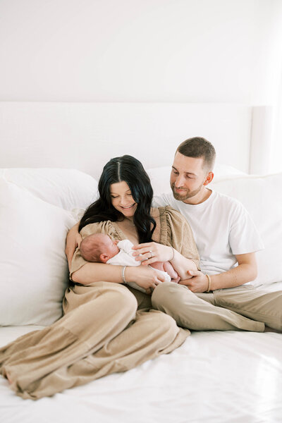Husband and wife lovingly cradle newborn son in their light-and-airy bedroom in Mechanicsburg, PA