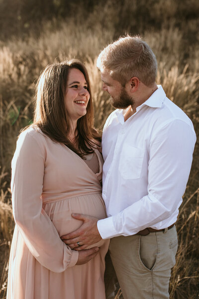 Pregnant woman looks at her husband as he gently touches her belly, her hand beneath his.