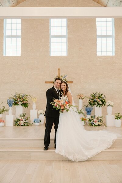 Bride and groom in chapel ceremony with bright colorful altar florals and blue cross backdrop
