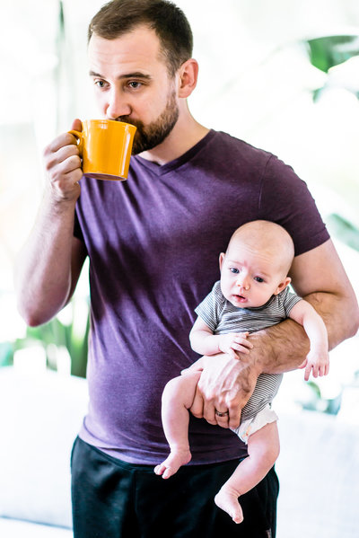 Dad drinking coffee from yellow mug while holding newborn