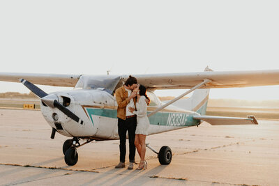Couple standing by an airplane kissing
