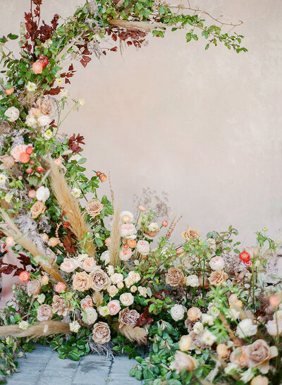 Dramatic floral installation wedding backdrop with greenery, peach, lilac and rust colored flowers