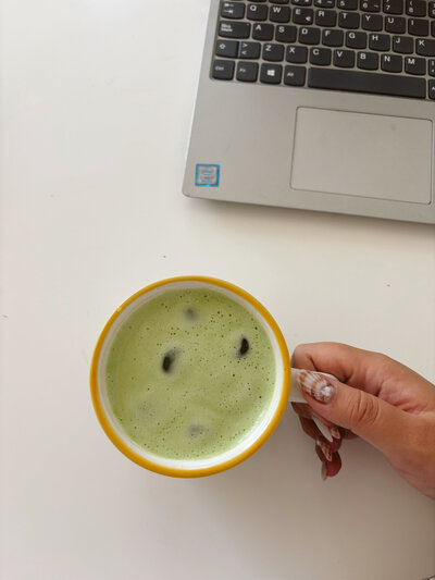 Hand holding a cup of matcha next to a laptop