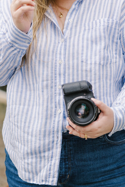 Close up of hands holding a camera in front of a blue and white striped shirt