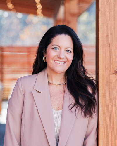 Alison Seponara in a pink blazer leaning against cedar post