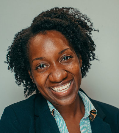 Professional portrait photo of Melanie Grandoit smiling and wearing a navy blue blazer with striped blouse. Melanie worked in corporate for 15 years.