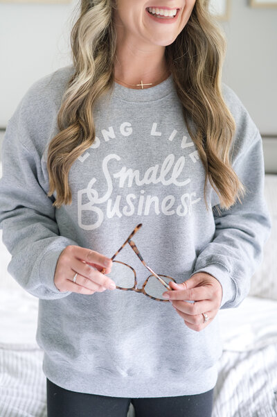 woman wearing long live small business sweatshirt holding blue light glasses