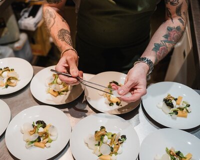 Chef using tweezers to plate delicate vegetable components on multiple white dishes at Sael Birmingham restaurant.