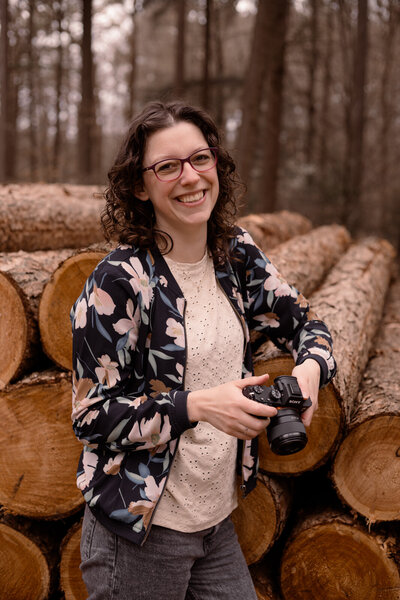 Joenne met fotocamera in haar hand  met een lach op haar gezicht in het bos in Apeldoorn
