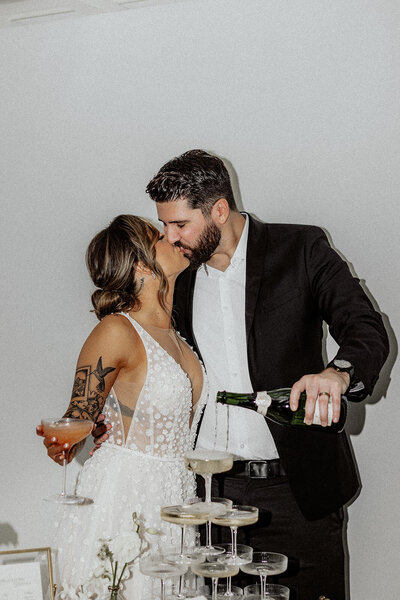 Bride and groom kissing while groom pours in the champagne tower in Las Vegas