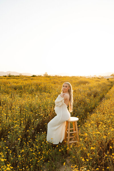 a pregnant woman sitting on a stool in a field of flowers