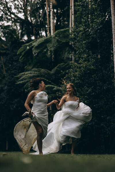 Queer bride and bride runing through the forest in the sunshine coast hinterland wearing their wedding dresses. Lesbian elopement 