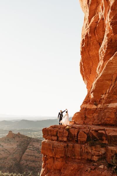 bride and groom holding hands while bride spins on the ledge of Cathedral Rock in Sedona Arizona with their elopement photographer