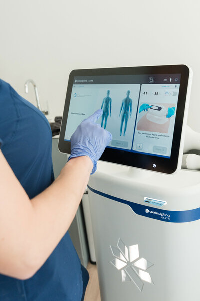  CoolSculpting treatments Dallas machine with a professional in a blue uniform organizing treatment and procedure details in a clinic setting.